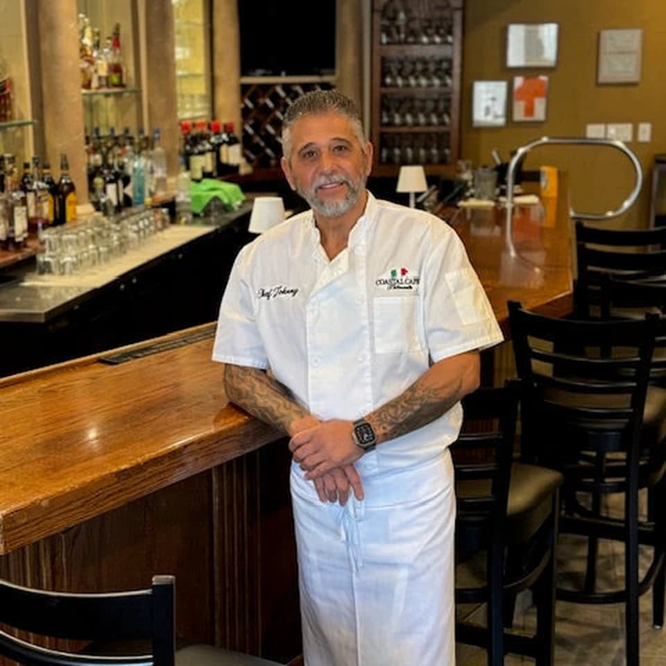 Chef Johnny Rovito in his chef's whites, leaning on the bar at Coastal Capri