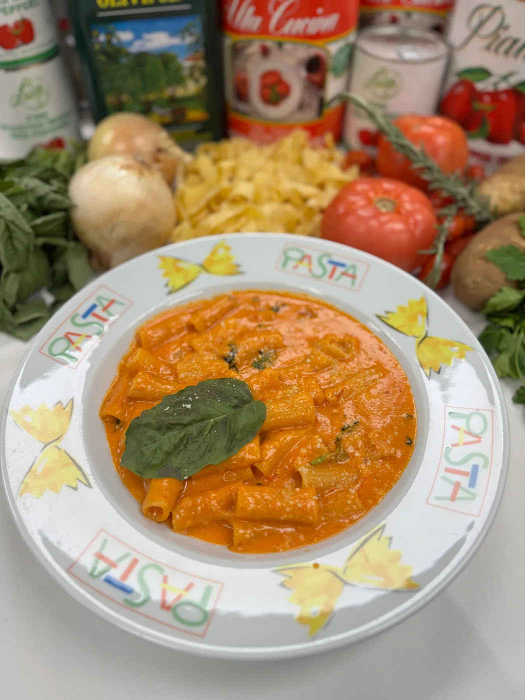 Rigatoni in pink vodka sauce with a basil leaf on a hand-painted pasta plate